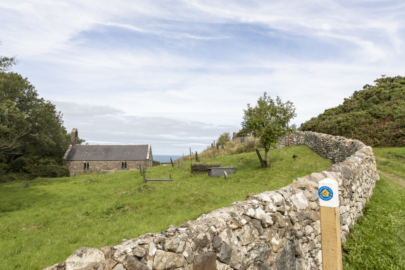 A view from over the low stone wall and through the graveyard of the 12th century, grade I listed church overlooking the sea.