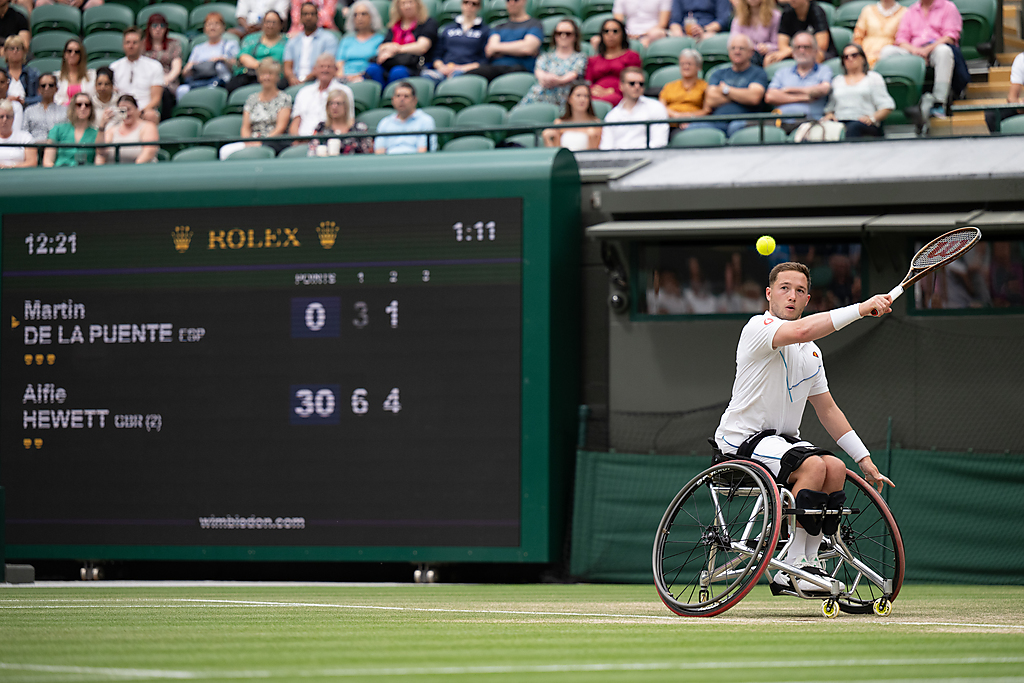"Image shows a tennis game between Martin De La Puente and Alfie Hewett, one player has his racquet raised and is about to hit the ball backhand"
