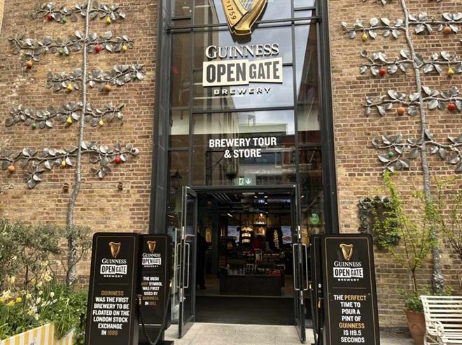 "Open glass doors and windows high above, standing banners to side of doors, sign above doors saying Guinness Open Gate Brewery, Brewery Tour and Store"