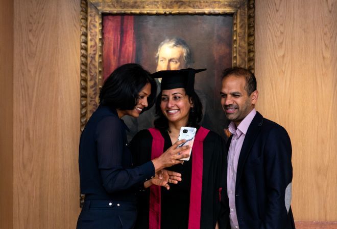 Photo of three people viewing a mobile phone and smiling 