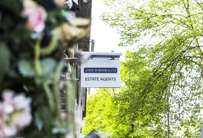 A sign for John D. Woods & Co Estate Agents hanging from a building