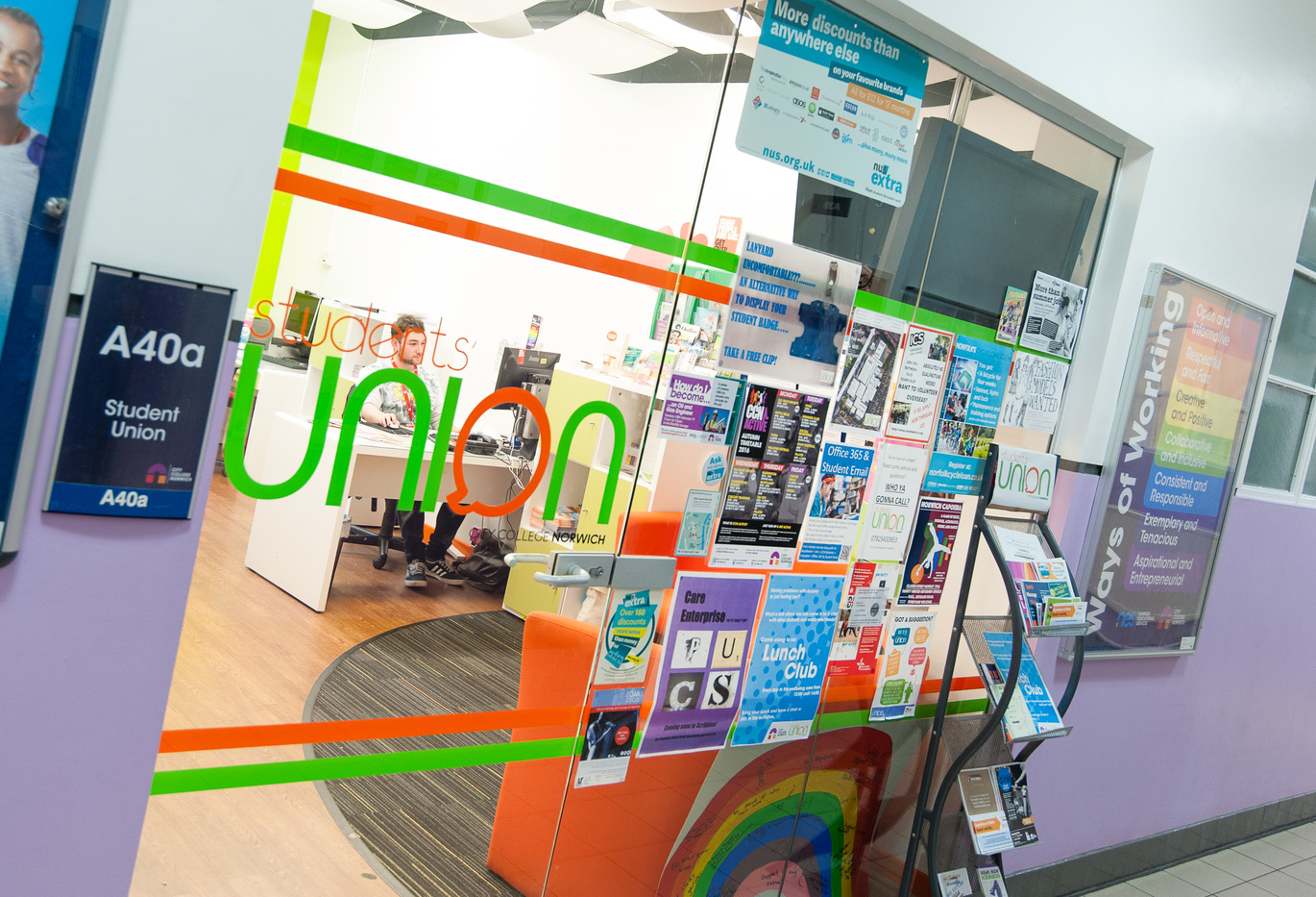 "Outside view of Student union looking inside where you can see leaflets, a white desk and a student"