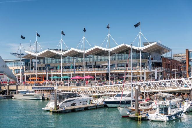 "Waterside view of Gunwharf Quays with marina, boats and modern shopping and dining buildings."