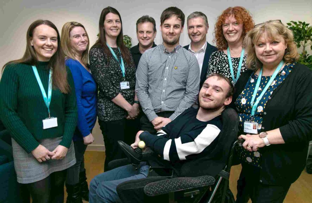 "Photo of 9 people smiling for a photo in an office environment. There are plants in the background."
