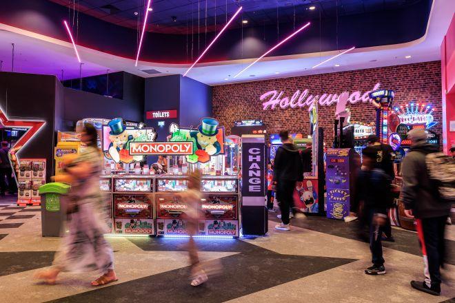 "Arcade area at Xscape with brightly lit gaming machines, including a Monopoly machine, and visitors walking past."