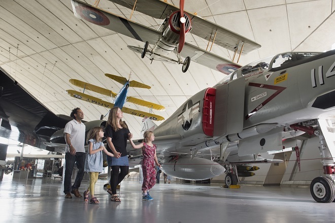 Photo of 2 adults and 2 children looking at side of plane inside a hangar.