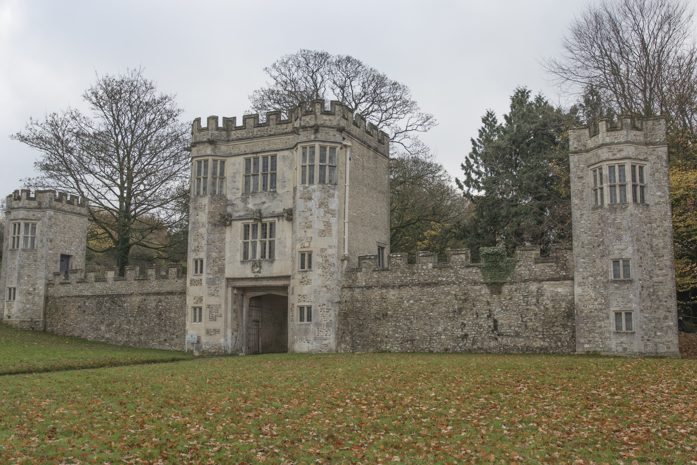 View of the medieval Gatehouse over the lawn with fallen autumnal leaves all over the grass and trees behind.