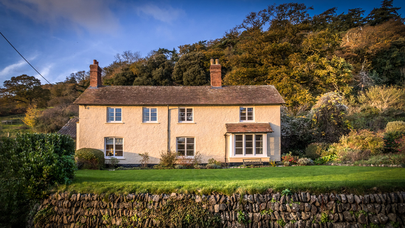 View over the wall and garden of Selworthy Farmhouse, surrounded by a forest of trees.