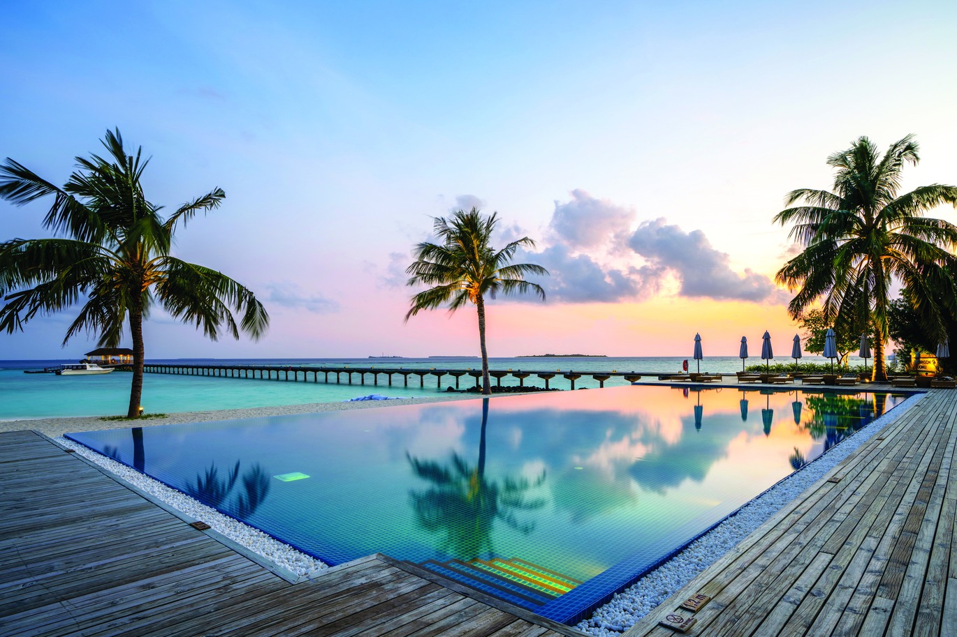 View of the infinity pool in the sunset overlooking the beach and blue sea.