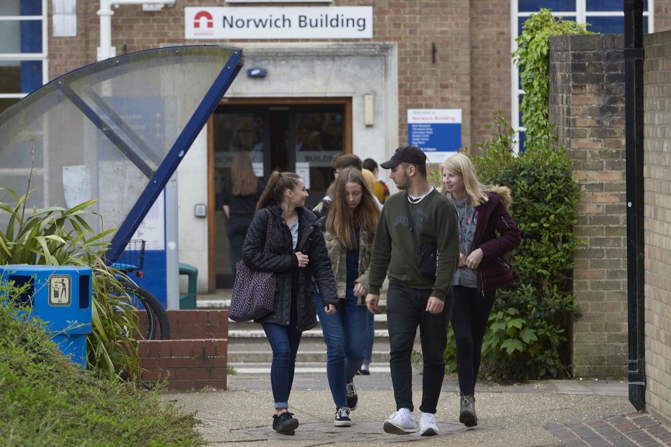 "Outside view of Norwich Building with 4 students walking past a glass shelter"