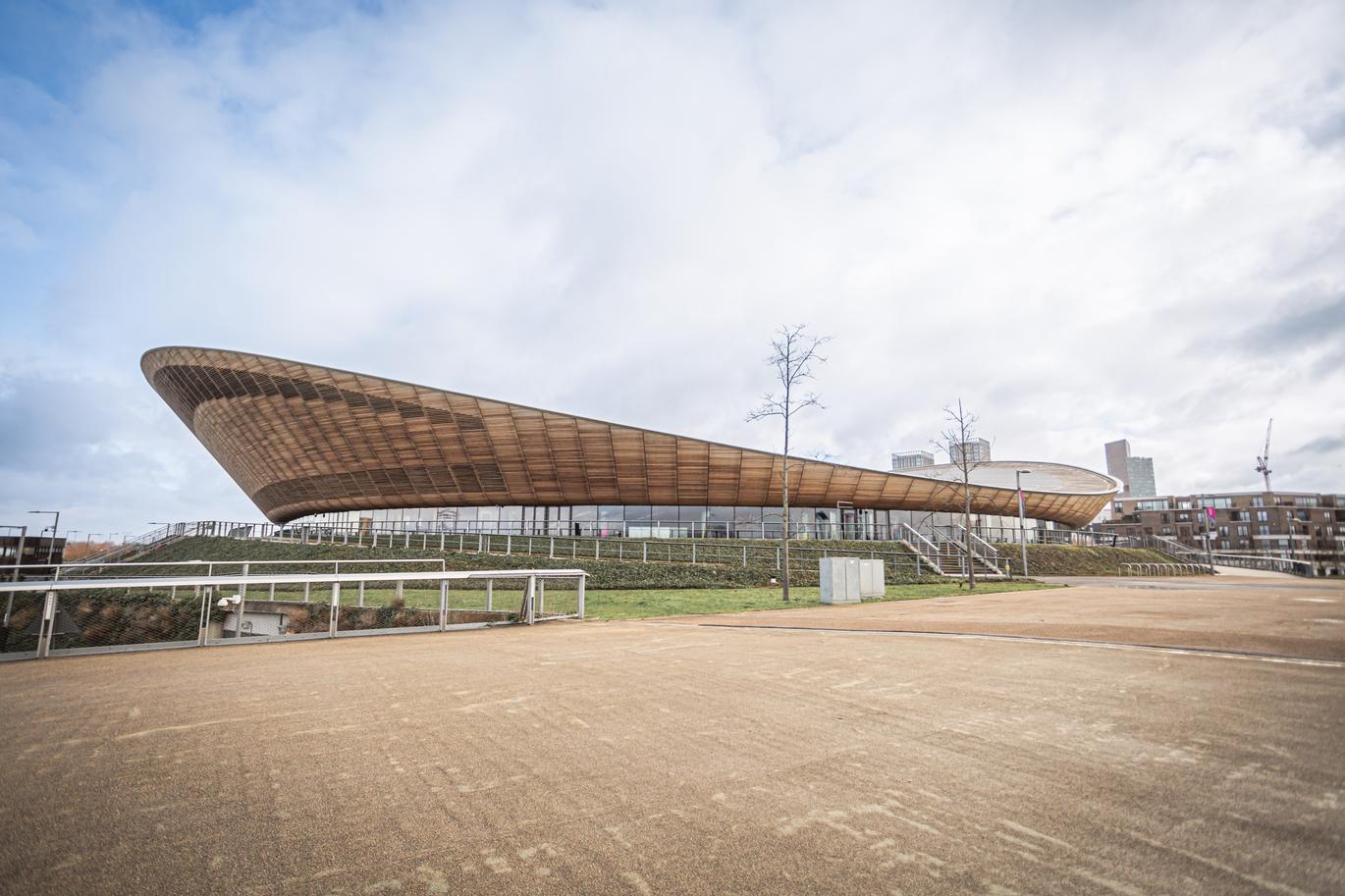 "Modern leisure building with a sweeping, curved roof and glass frontage, set on landscaped grounds beside a wide paved area."