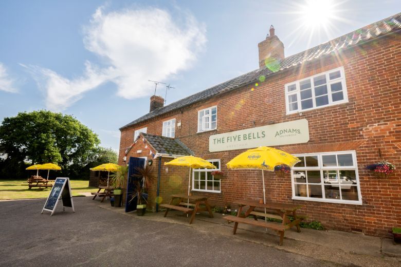 "External view of The Five Bells, outdoor seating benches with umbrellas and a sunny blue sky with a couple of clouds"