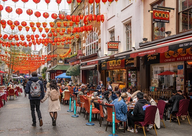 "There are lots of people sitting outside eating at tables outside a Chinese restaurant named Four Seasons."
