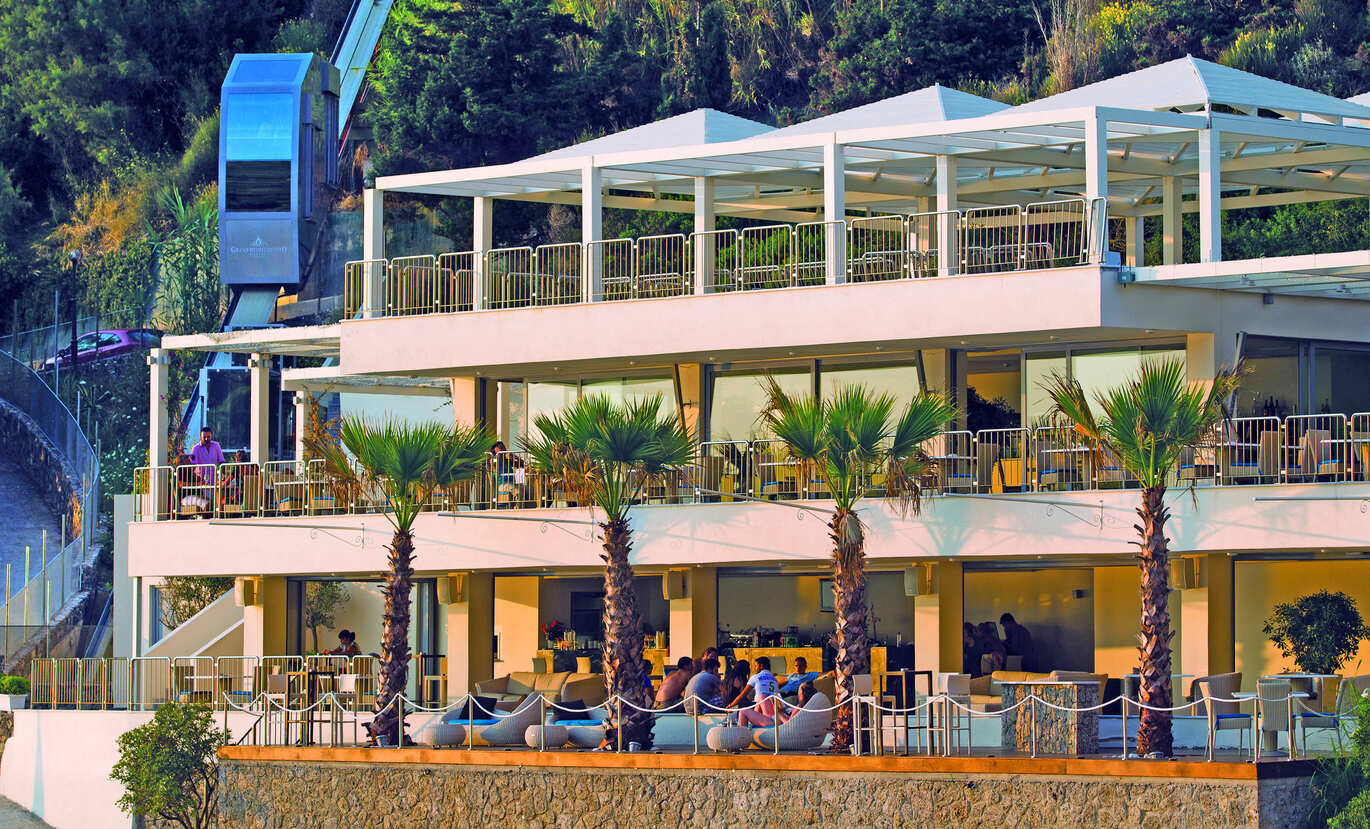 View of the 3 story bar and restaurant area right on a cliff face with trees behind and a lift going up behind.