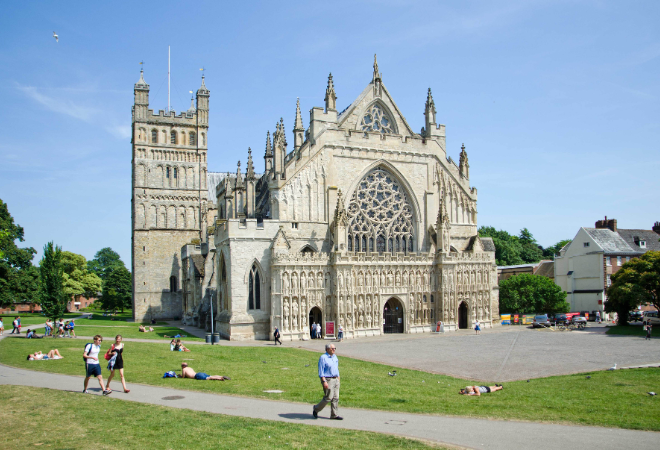"Exeter Cathedral surrounded by blue skies and people chilling on the grass in front of the Cathedral"
