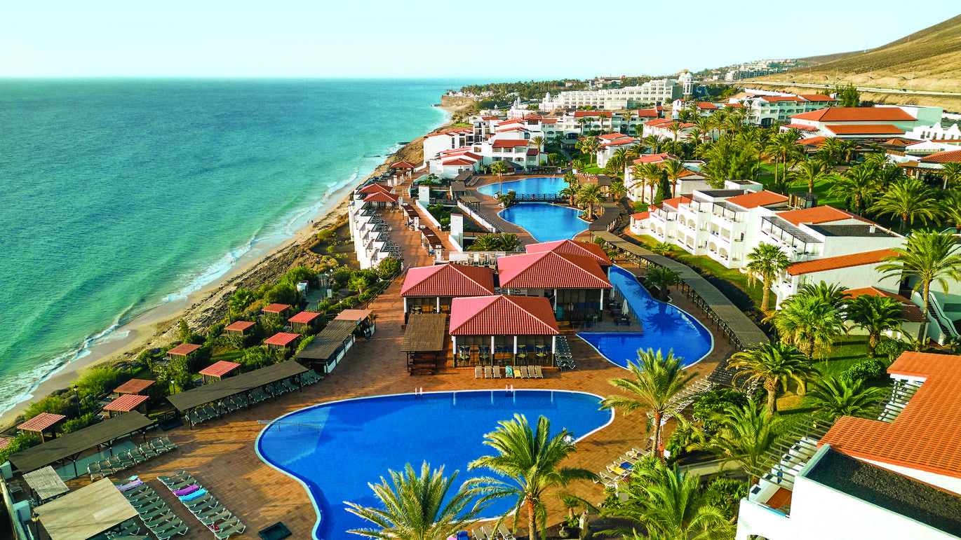 Aerial view of the hotel complex with a number of pools surrounded by buildings and palm trees, right on the beach.