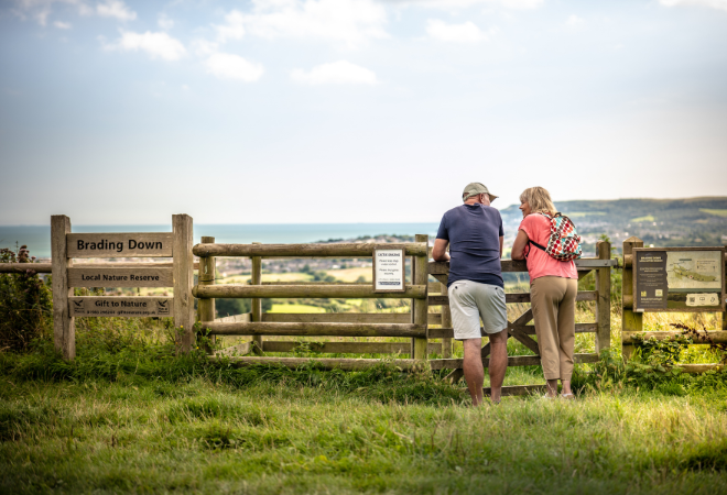 "A male and a female leaning up against a fence at Brading Down whilst on a countryside walk"