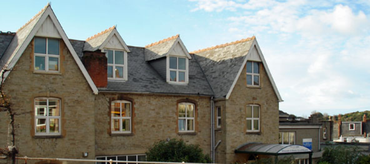 An outside view of the upper stories and roof of a light-brick building. A sheltered entryway on the ground floor on the right hand side. 