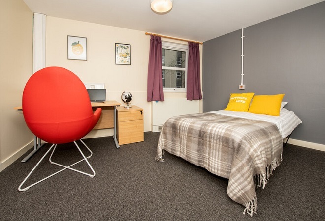 "Image of bedroom with a bed, desk and large orange chair"