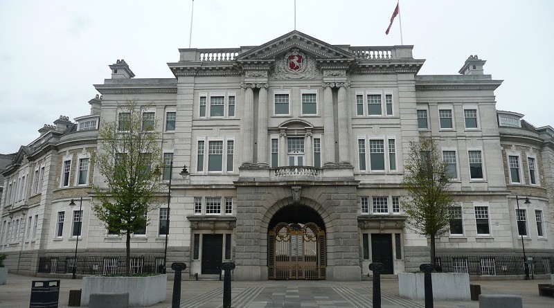 "Grey building with archway entrance and pedestrianised area in foreground."