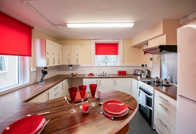 "Image of a kitchen with a dining table set with red glasses and crockery and a kitchen worksurface in background"