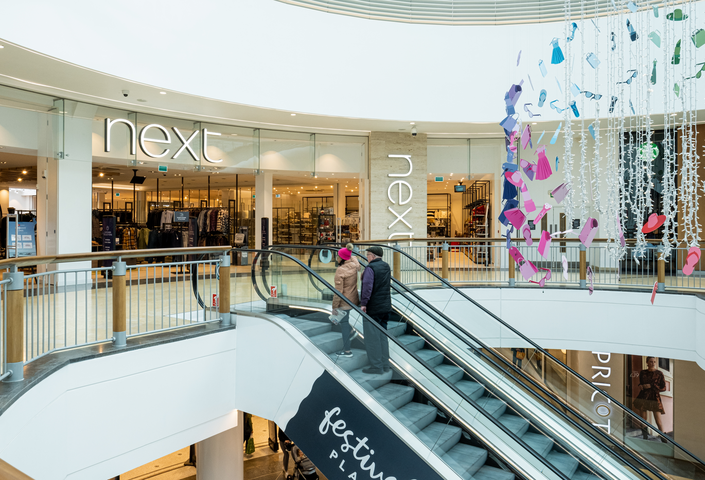 "Image depicts two people ascending on an escalator toward the entrance to Next on the upper level of the shopping centre"