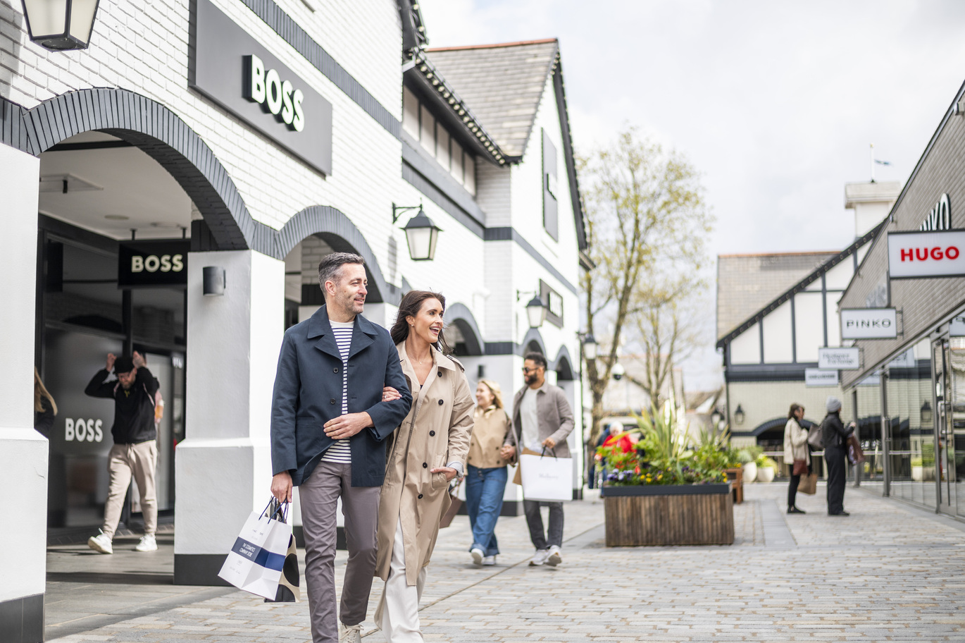 "Two people walking with shopping bags outside a shop labelled Boss"
