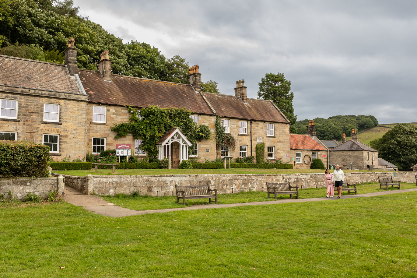 "Converted houses at Danby Lodge with a grass area to the front containing a path and benches. Two people walk along the path taking in the sights"