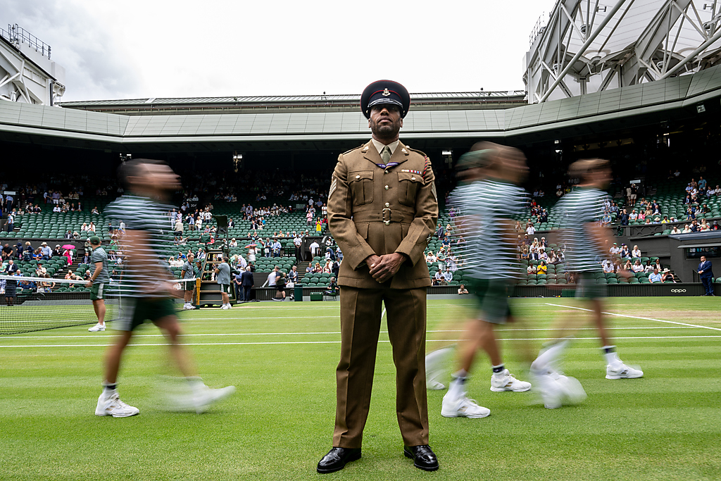 "Photograph shows a member of the Army stewarding at the Wimbledon Championships with blurred images of ball boys walking behind him on one of the courts as Wimbledon"