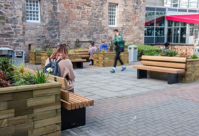 "Outdoor communal student area with student walking and student sitting on bench"