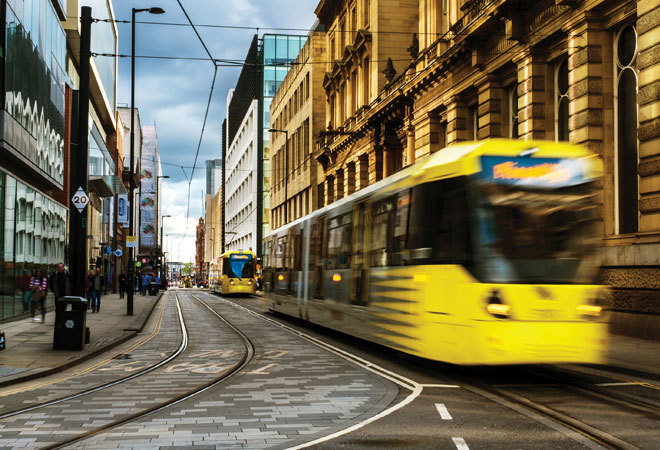 photo of two trams moving through manchester. the closest tram is blurred due to movement.
