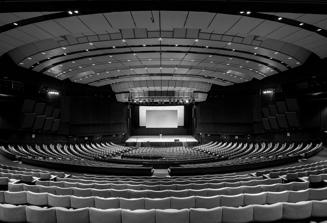 "A photograph of one of Harrogate Convention Centre's exhibition spaces.  This is an auditorium with a centre stage surrounded by seating". 