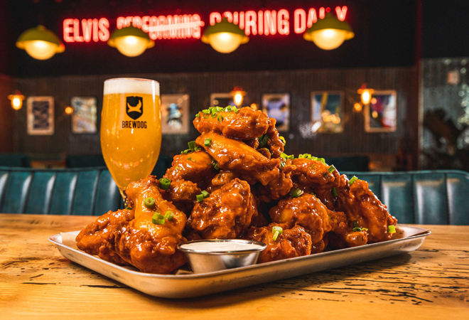 "Close up photo of hot chicken wings, covered in sauce and chillis, served with a Brewdog Beer"