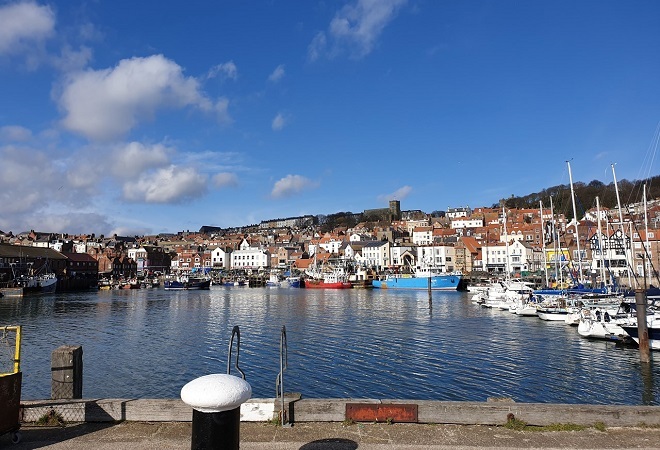 LEISURE BOOTS MOORED AT A DOCKYARD, HOUSES ATOP HILLS AND BEAUTIFUL BLU SKY WITH A FEW CLOUDS DOTTED AROUND