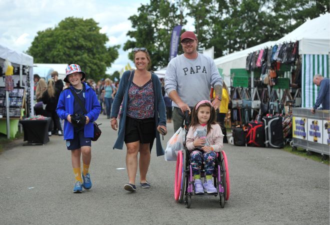 "A Male, female and a female wheelchair user travelling along a path at one of the events, past the stall holders"