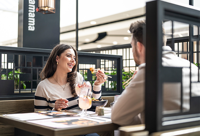 "Image of two people sitting in a booth at Wagamama eating food"