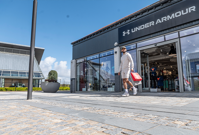 "A man outside a shop called Under Armour while holding shopping bags"