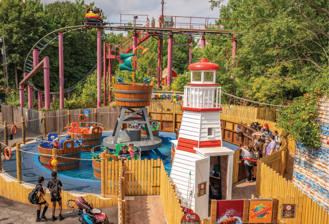 "image of the ride Barrel Bail Out showing a white light house, and the barrels of the ride"