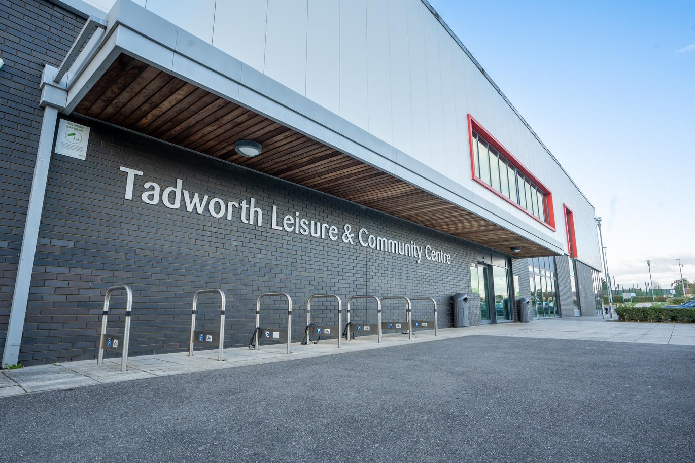 "Exterior of Tadworth Leisure & Community Centre with signage on a brick wall, bike racks, and a modern entrance."