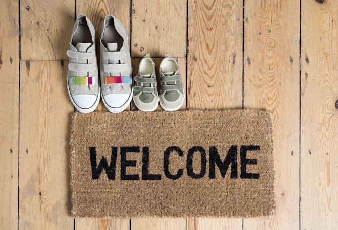"A doormat with the word Welcome on it. Two pairs of shoes together just overlapping the matt"