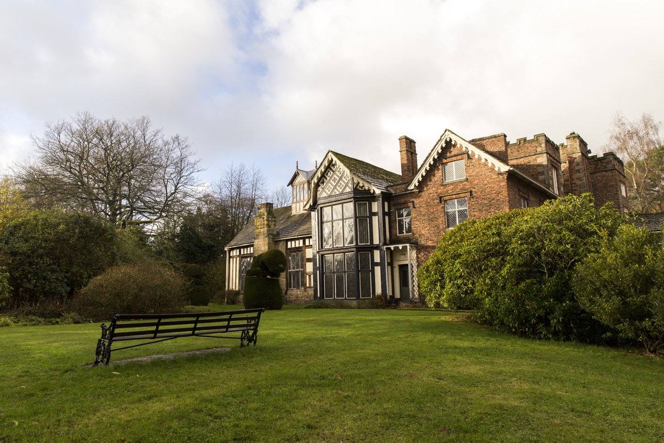 View of the 16th century Rufford Old Hall surrounded by trees and a small green lawn out the front with a single bench.