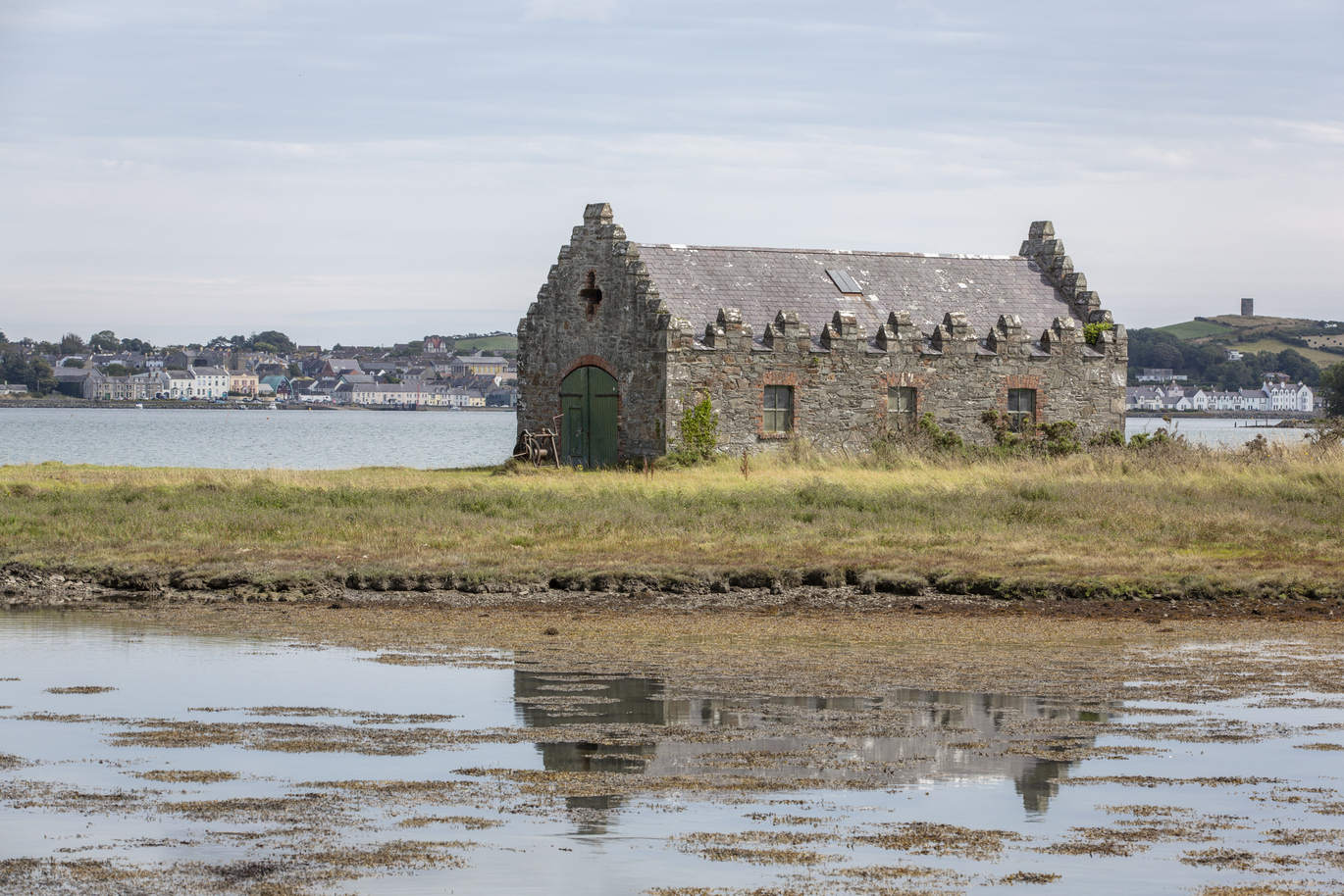 View of the 18th century boathouse on Strangford Lough surrounded by water with buildings in the background the other side of the water.