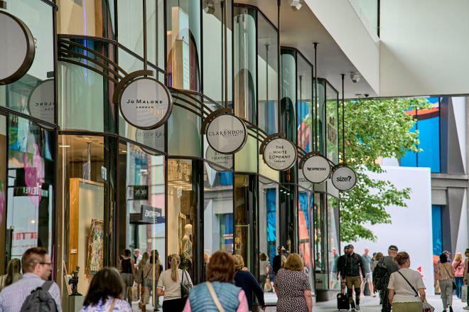 "Liverpool ONE shopping arcade with glass-fronted stores and circular hanging signs above busy walkway."