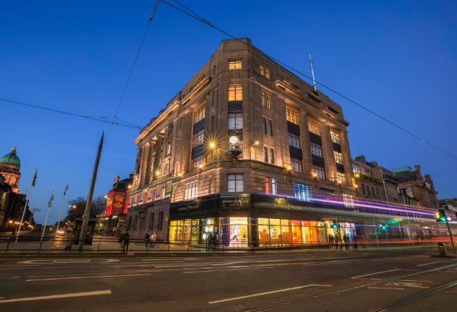 "view from across the road of Johnnie Walker, Princes Street. Late evening, and traffic blurs as it passes by"