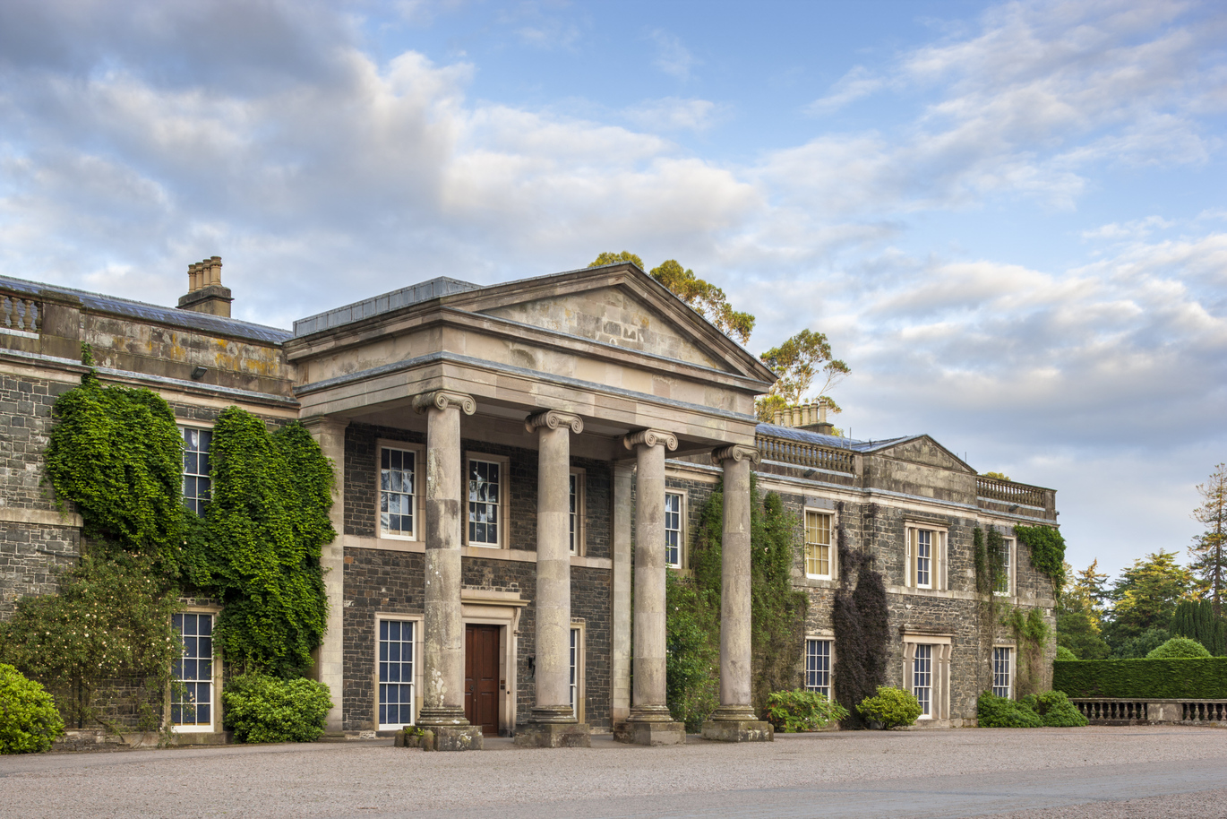 The front of the 19th century large Mount Stewart mansion, with greenery climbing up the building and 4 large stone pillars at the entrance.