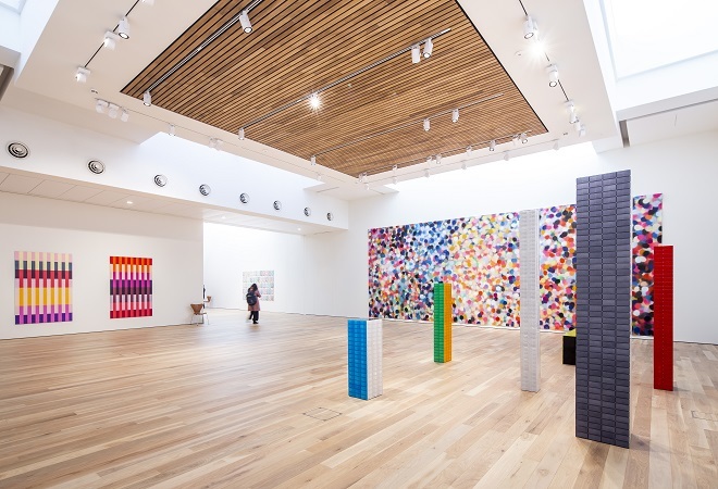 "Photo of gallery inside with colourful artwork on the wall and block towers in the floor."