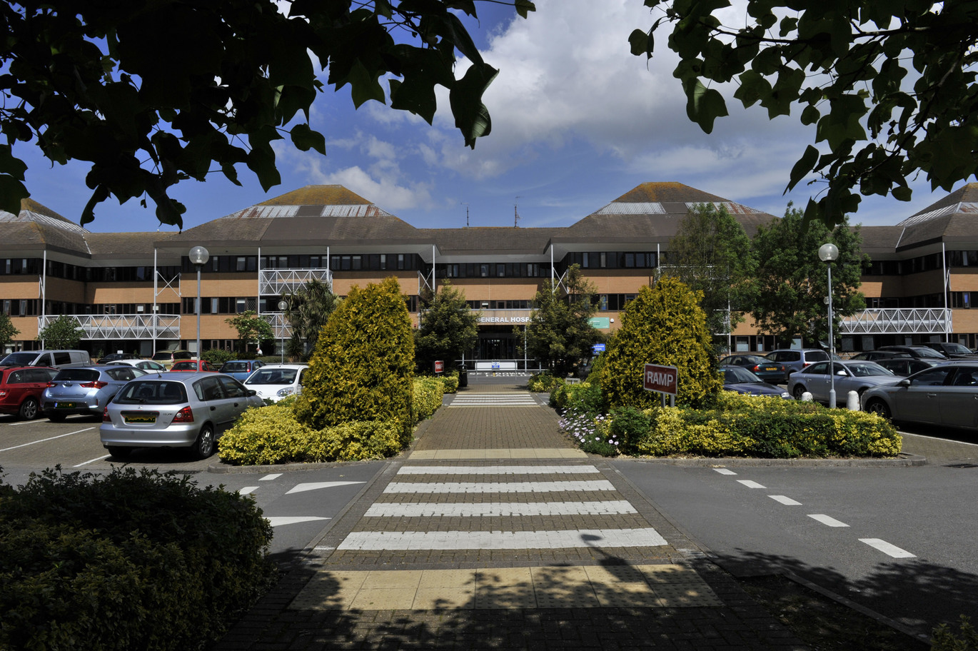 Horizontal shot of full Weston and General Hospital car park with zebra crossing and foliage with hospital building at the back.