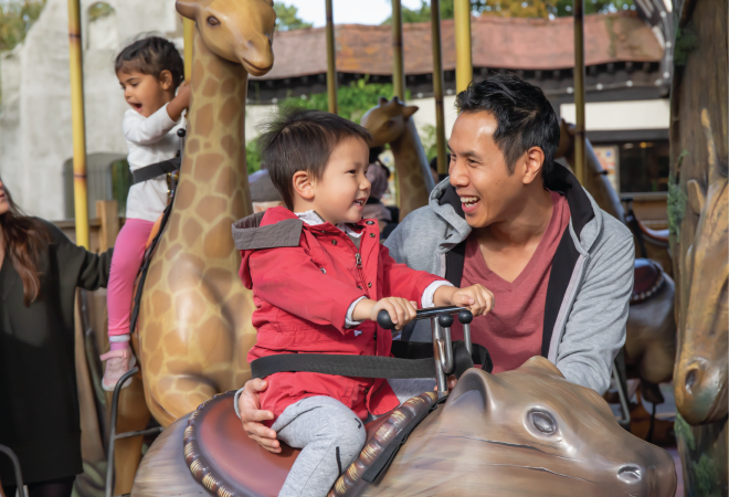"A child is sitting on a ride, with an adult smiling with them"