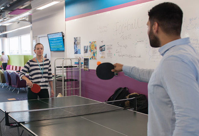 two student are playing pingpong in a common room.