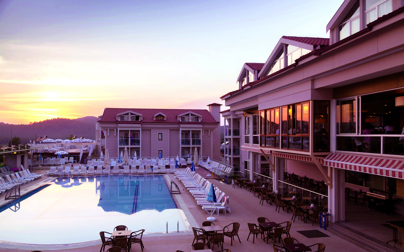View of the pool area in the sunset with sun loungers surrounding the pool and the hotel buildings behind.